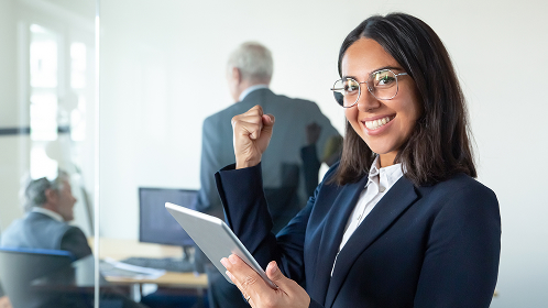 happy-female-professional-glasses-suit-holding-tablet-making-winner-gesture-while-two-businessmen-working-glass-wall-copy-space-communication-concept 1