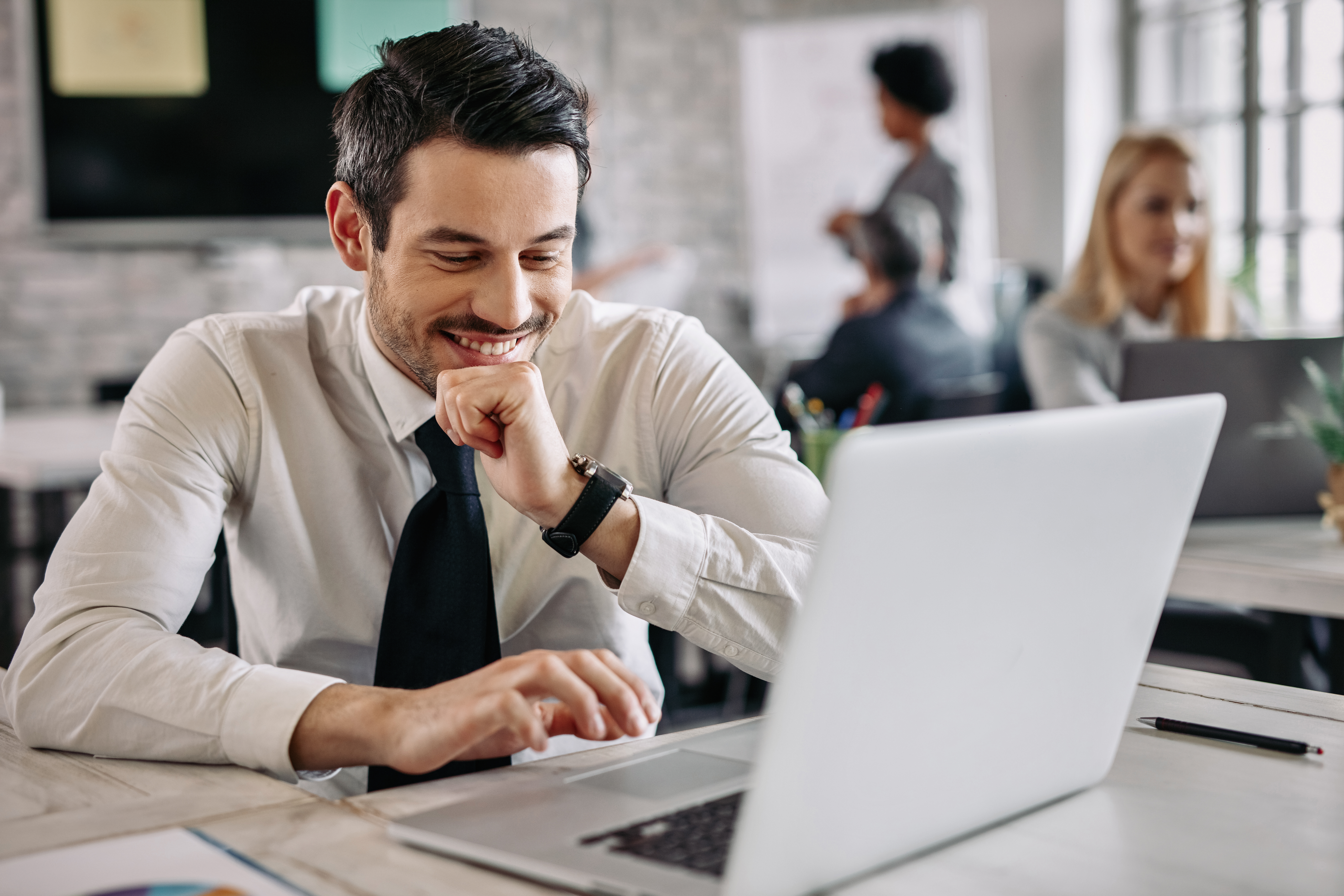 smiling-businessman-sitting-desk-office-working-laptop-there-are-people-background-1